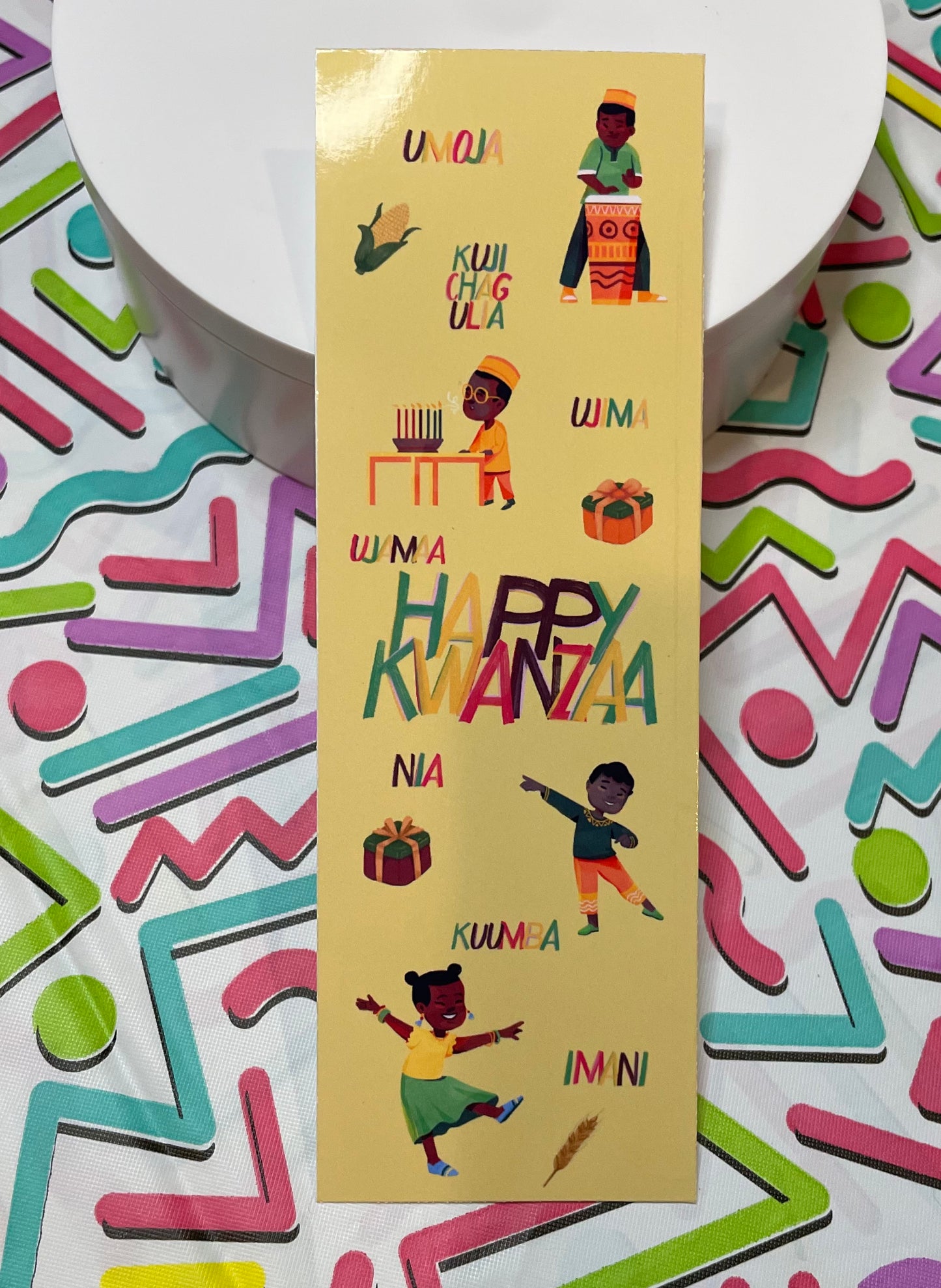 A colorful bookmark featuring illustrations of African children and the seven principles of Kwanzaa, with a gold glossy finish.