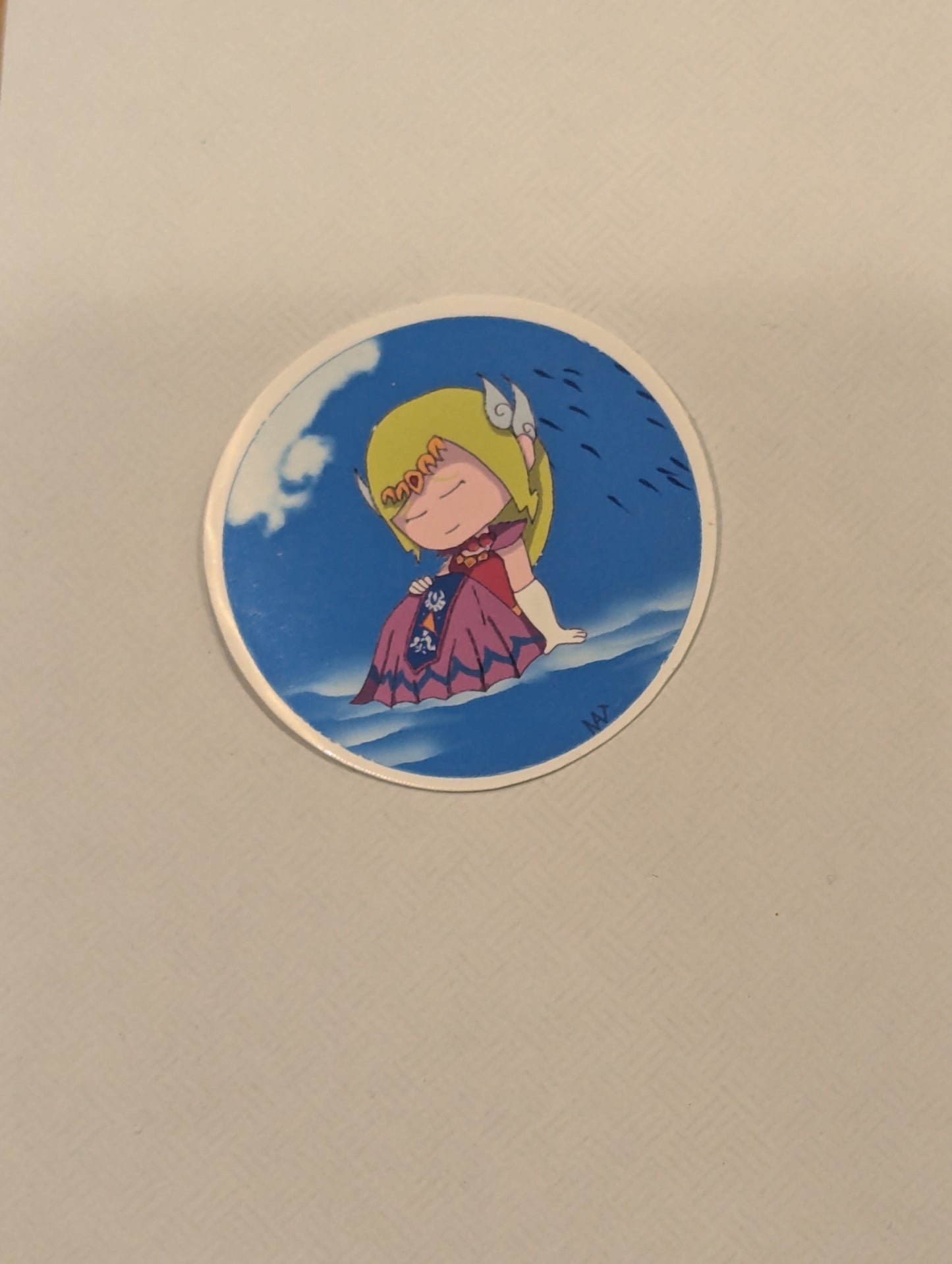 Circular sticker with a character in a purple dress and yellow headscarf on a blue background, attached to a beige surface.