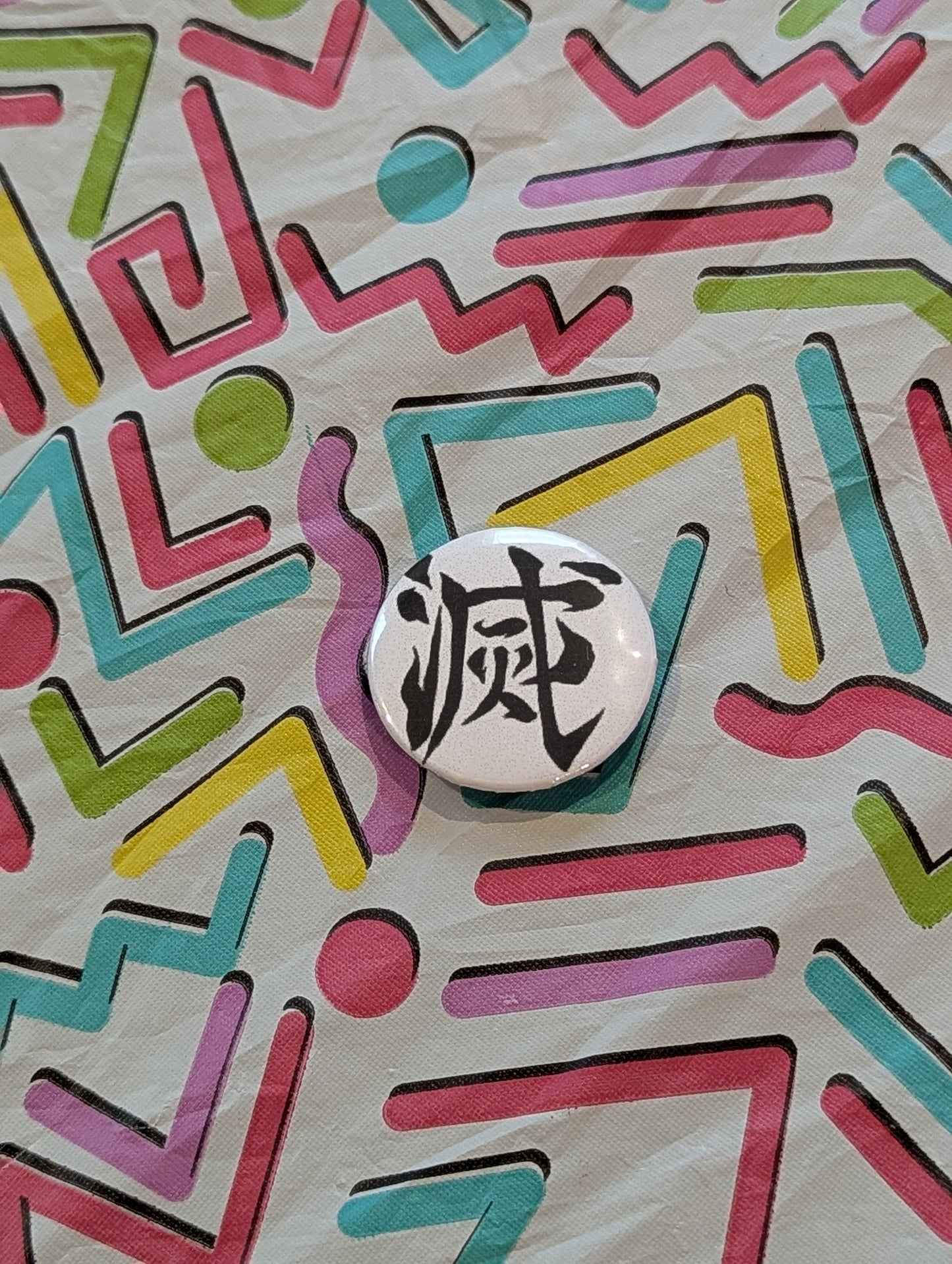 Demon Slayer Button with black text on a colorful geometric patterned background