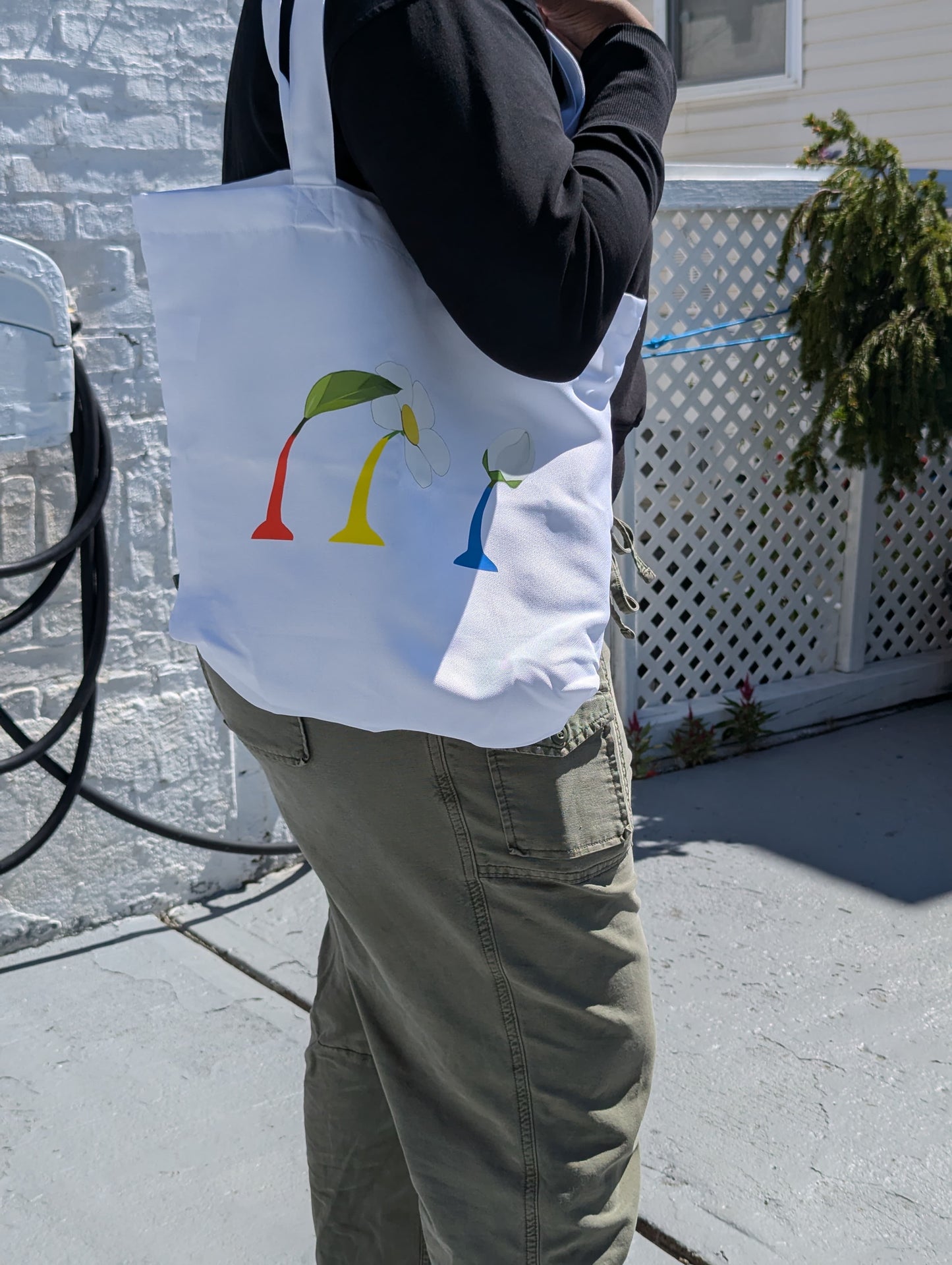 Person holding a white tote bag with colorful designs outdoors.