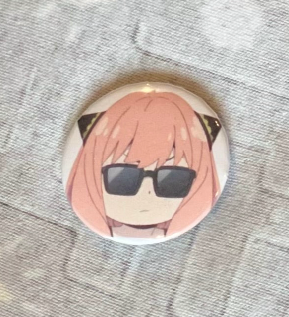 Button badge with an anime character wearing sunglasses on a textured surface