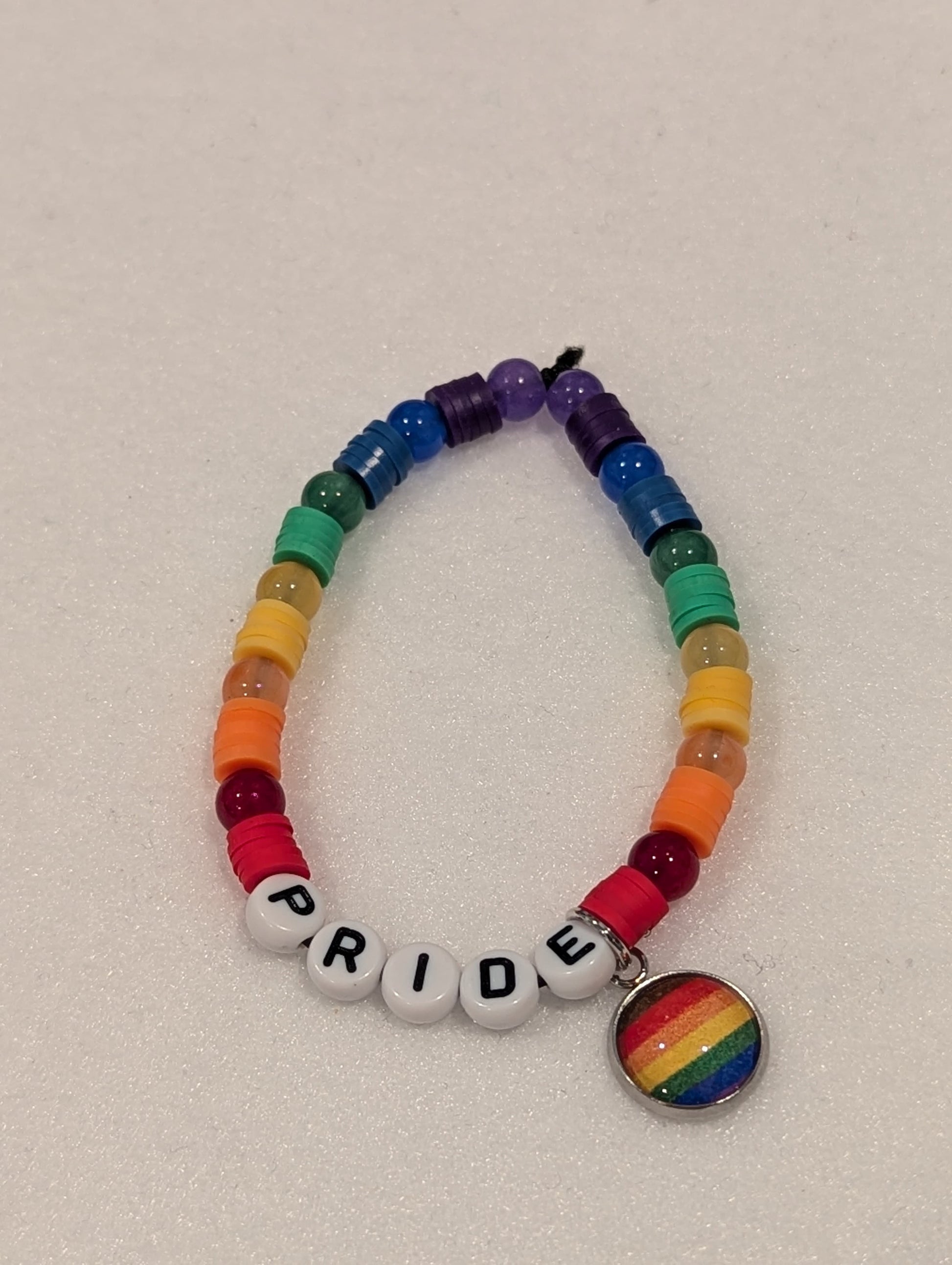 Rainbow beaded bracelet with 'PRIDE' beads and a rainbow charm on a light gray background