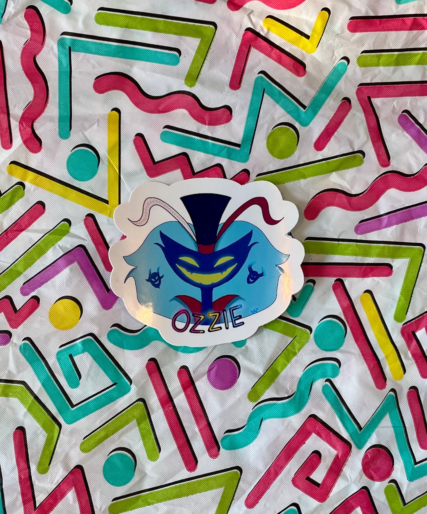 Colorful geometric patterned paper with a sticker of a blue mask labeled 'OZZIE'.