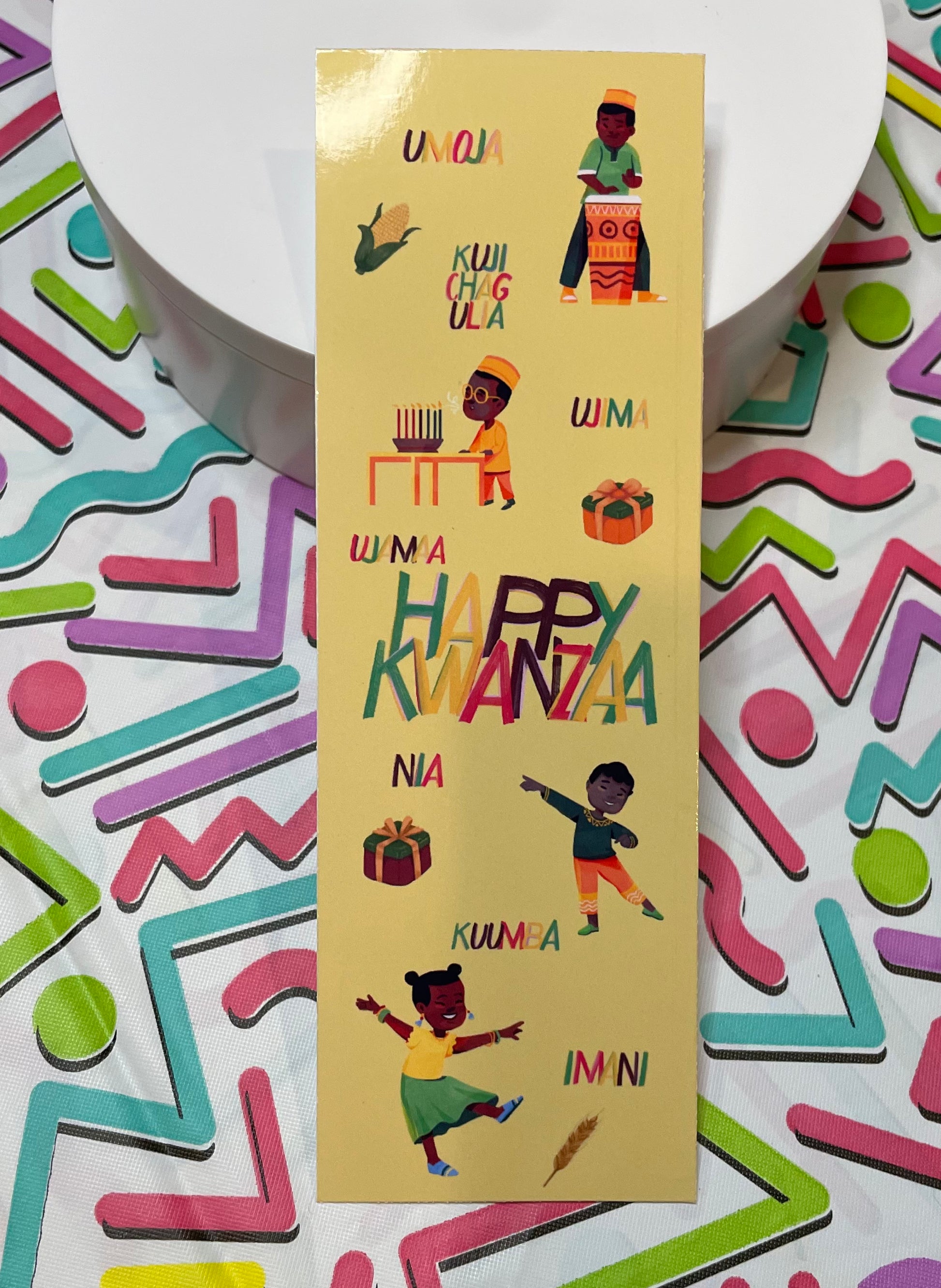 A colorful bookmark featuring illustrations of African children and the seven principles of Kwanzaa, with a gold glossy finish.
