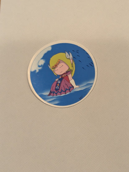 Circular sticker with a character in a purple dress and yellow headscarf on a blue background, attached to a beige surface.