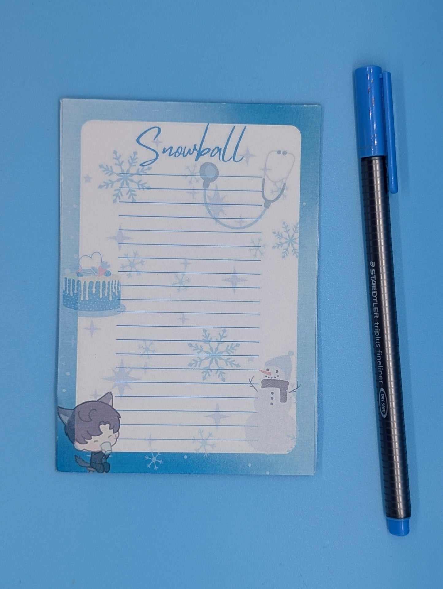 A notepad with a blue and white design featuring snowflakes and a character illustration from a mobile game, accompanied by a blue pen.
