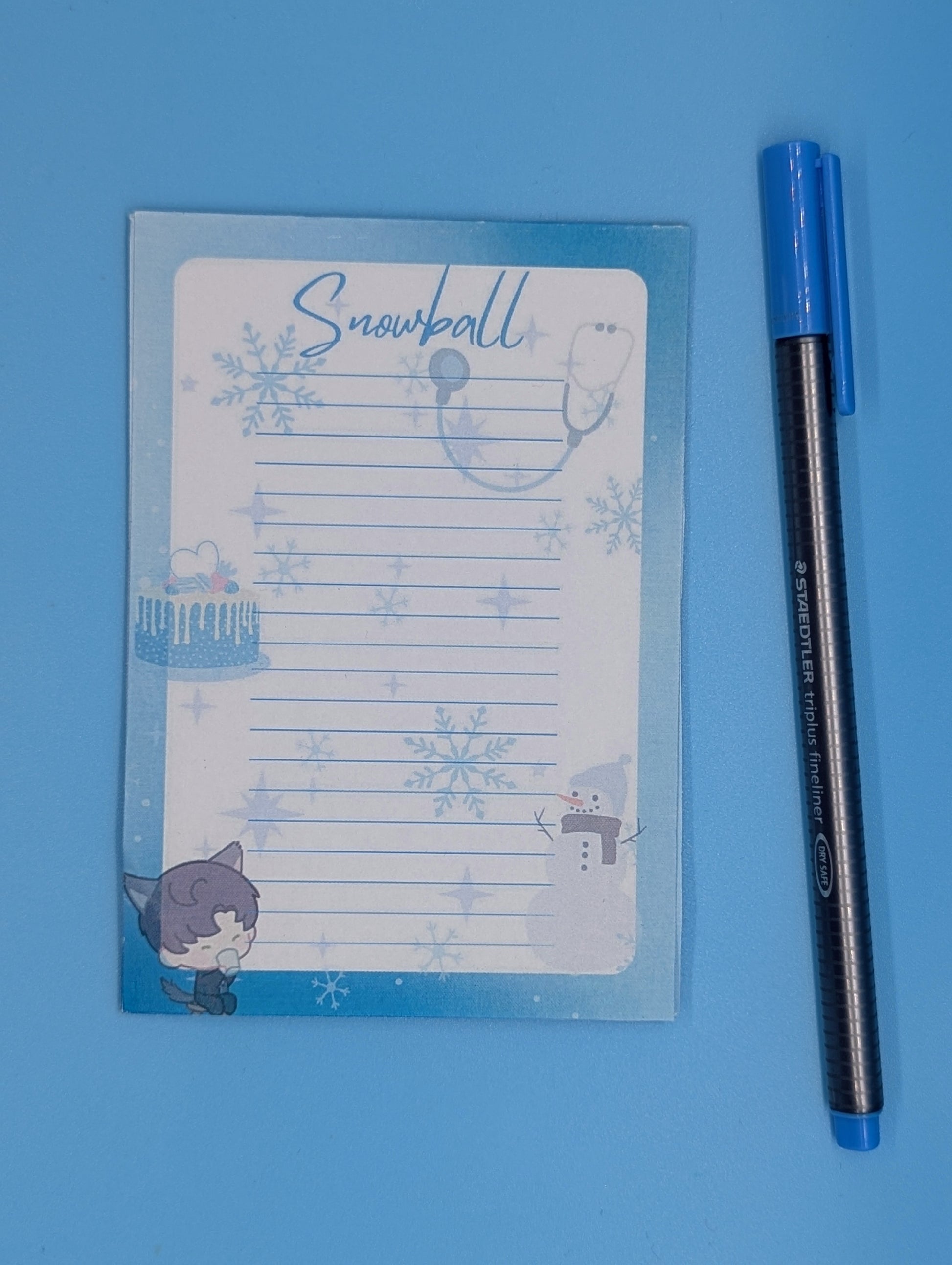 A notepad with a blue and white design featuring snowflakes and a character illustration from a mobile game, accompanied by a blue pen.
