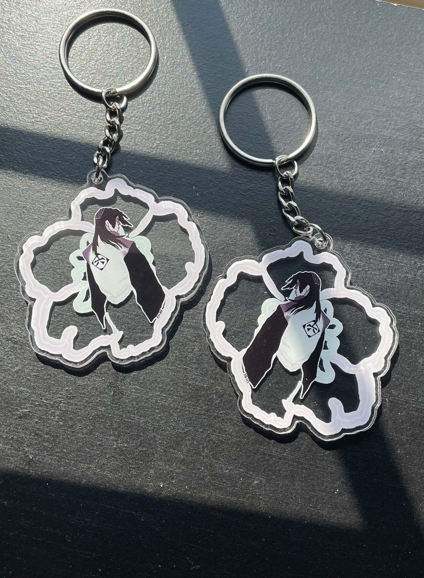 Two keychains with a design of a person in a cloud on a dark surface.
