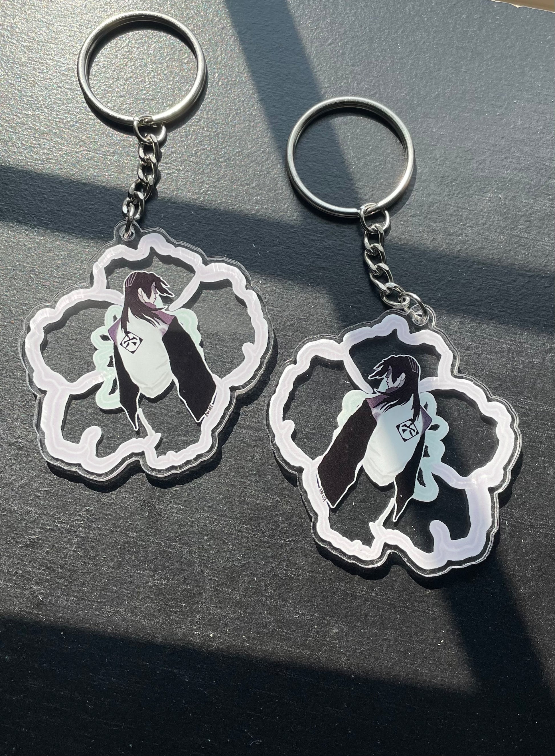 Two keychains with a design of a person in a cloud on a dark surface.